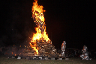 The effigy burns while fire guardians look on.
